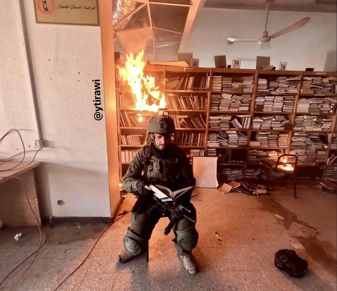 An Israeli soldier poses in front of Al-Aqsa University library, which they set on fire.